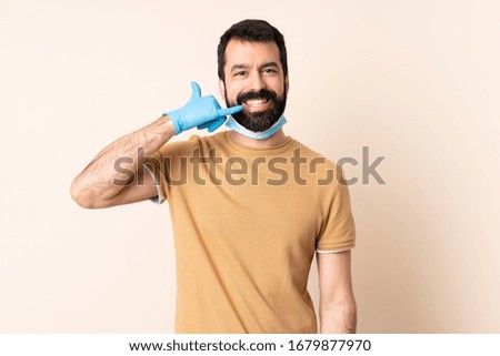 Caucasian man with beard protecting from the coronavirus with a mask and gloves over isolated background making phone gesture. Call me back sign