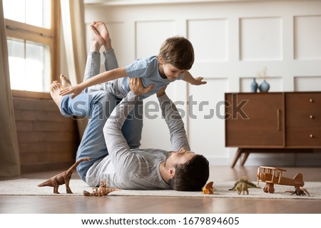 Happy young father lying on floor in living room hold fly with little preschooler son engaged in funny game together, loving dad relax playing with small boy child, enjoy family weekend at home Royalty-Free Stock Photo #1679894605