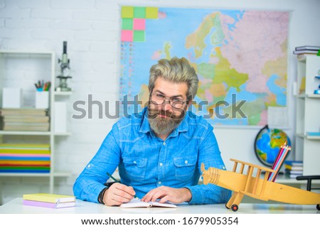 Bearded professor at school lesson at desk in classroom. School concept. Exam in college. Teacher working at table in classroom. Handsome male primary school teacher in classroom. Back to school.