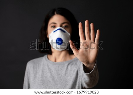 young woman in mask is making stop hand sign. black background
