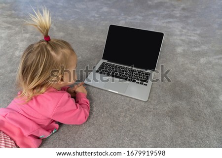 Small cute blond caucasian child laying on floor on grey rug and watching cartoons on laptop. black screen, mockup, copy space,view from top.