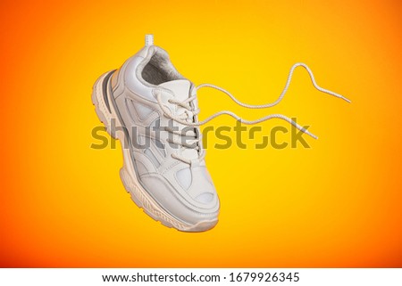 One sneaker is hanging in front of colorful background. One sneaker shoe on yellow background flies in air.