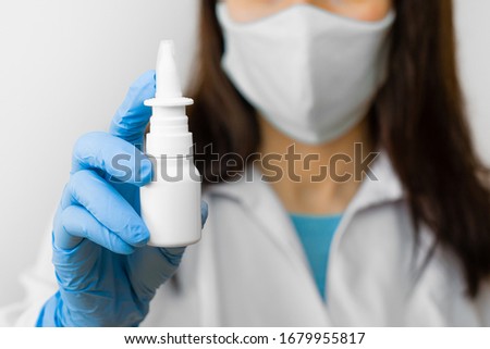 A woman using nose spray for flu treat or running nose holds medicine in the hand. Doctor in protective mask and blue gloves shows nose spray for illness treatment. Royalty-Free Stock Photo #1679955817