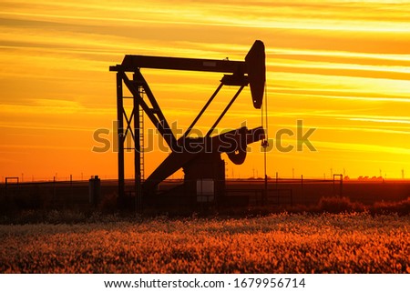 Silhouetted pumpjack in the oil field at sunset