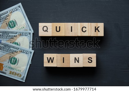 Modern business buzzword - quick wins. Top view on a black board with dollars and wooden blocks. Close up. Top view.