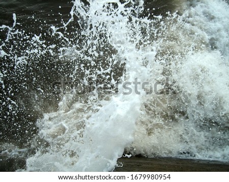 Sea waves of dark water beat against the coastal rocks. An infinite number of splashes, drops of water and white foam are scattered.
