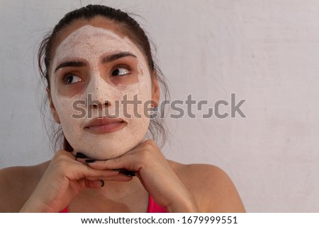 portrait of young hispanic woman wearing a hydrating and exfoliating face mask on a white background