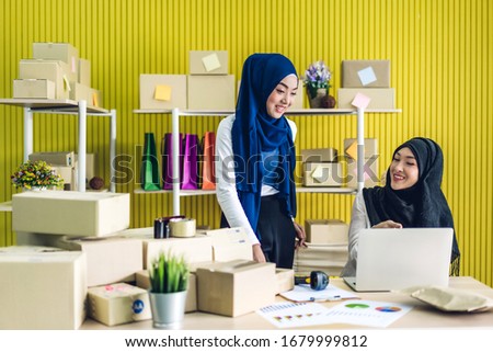 Portrait of smiling beautiful two muslim owner asian woman freelancer sme business online shopping working on laptop computer with parcel box on table at home - Business online shipping and delivery