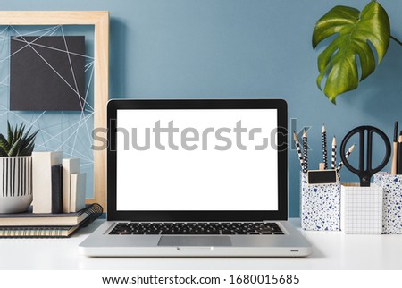 Home office creative desk with laptop, notice board and blue wall.