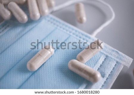 Surgical mask and few tablets with container lies on white background. Mask should protect against viruses and pills increase the immune system.