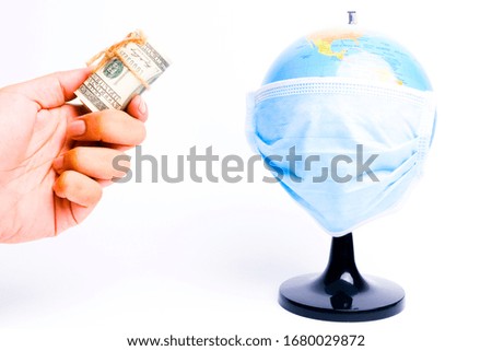 A picture of hand holding money with globe wearing medical mask. World need aid in terms of monetary in combating covid 19.