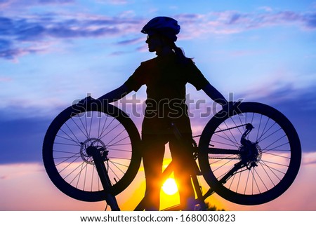 Silhouette of a girl cyclist with a Bicycle in his hands against the sunset. Sports and recreation. Hobbies and health. Nature and man