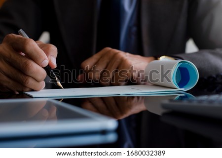 Closeup business man hand write and sign empty white cheques with  modern tablet computer pc and laptop computer on the desk at office. Paycheck and payroll concept. 