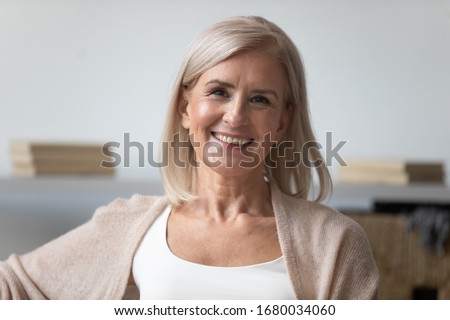 Head shot close up portrait of pleasant smiling mature woman. Happy healthy middle aged lady relaxing alone at home, looking at camera, posing for photo. Positive satisfied retirement concept. Royalty-Free Stock Photo #1680034060