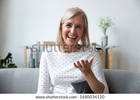 Happy mature blonde lady sitting on couch, holding video call with friends, head shot close up portrait. Web cam view laughing middle aged woman having fun, talking with grown up children online. Royalty-Free Stock Photo #1680034120