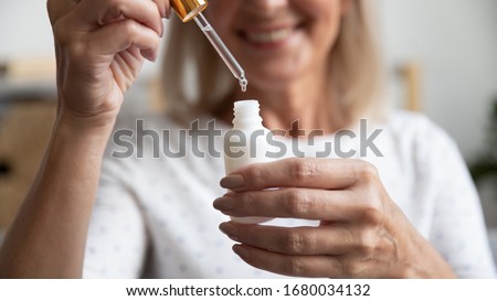 Close up happy older woman opening bottle with essence, pipetting skincare product. Smiling middle aged lady using pleasant fragrance liquid or antiaging moisturizing oil, beauty procedure at home. Royalty-Free Stock Photo #1680034132