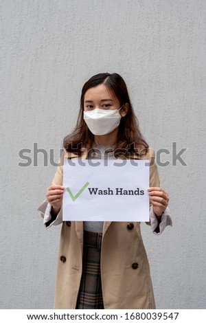 A Chinese woman wearing face mask and holding a "Wash Hand" sign.
