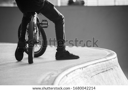 Cyclist with a BMX bike resting next to a ramp photographed in black and white.