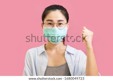 Young asian woman wore a gray undershirt, Blue shirt and protective masks against virus and air pollution,make gesture raise her fist,fight isolated on pink background,health care concept