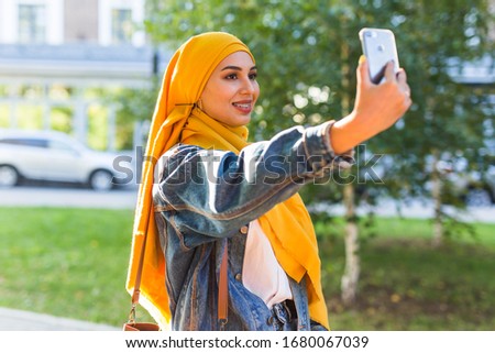 Muslim girl in hijab makes a selfie on the phone standing on the street of the city