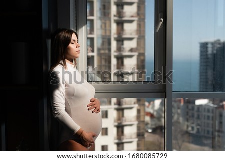Happy parents. expectant mother with a big belly is standing at the window. Expecting a baby. T