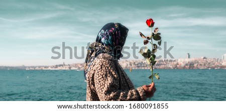 An unidentified muslim woman holding a red rose by the Bosphorus Strait of Istanbul. Royalty-Free Stock Photo #1680091855