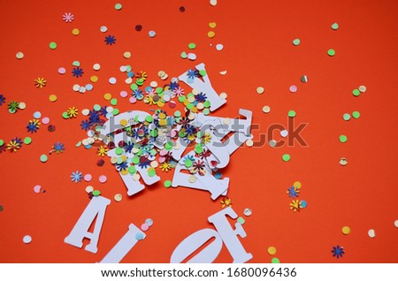 carved letters of the day of the fool mixed with multicolored confitti on an orange background