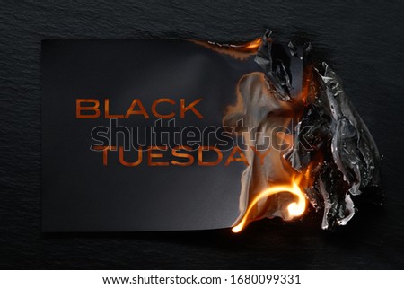 Burning piece of black paper with the word "Black Tuesday"on a black background.