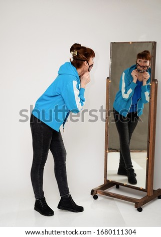 Photo woman in a mask in a blue blouse and jeans on a white background in full growth looks in the mirror