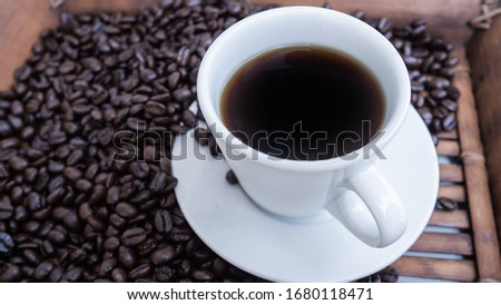 close up black coffee beans on a wood background with white coffee cup.