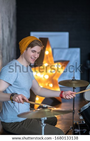 Feeling great. Young man in an orange hat looking amused while playing the drums