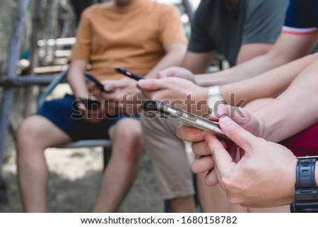 Closeup group friends hands holding modern smartphone chatting in the park.
Young friends watching social media video on mobile cell phone outdoors.
Friendship people together online internet concept.
