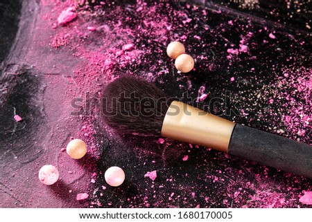 A make-up brush with crushed cosmetics and pearls on a dark background, with a place for text