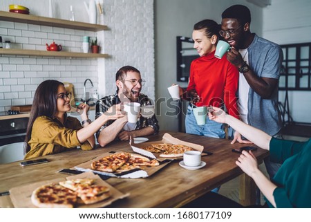 Joyful young multiethnic people in casual clothes relishing of pizza and drinks while celebrating birthday and proposing toasts at cozy kitchen Royalty-Free Stock Photo #1680177109