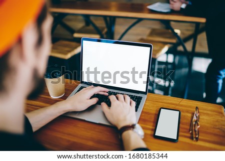 Cropped back view of millennial freelancer searching web information on mock up laptop computer with copy space area, skilled man using modern netbook and smartphone technology with blank screens