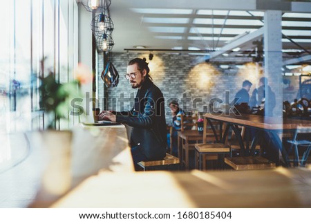 Side view of skilled male freelancer doing remote work during online browsing on modern netbook, millennial programmer creating database on laptop computer connected to wifi internet in coffee shop