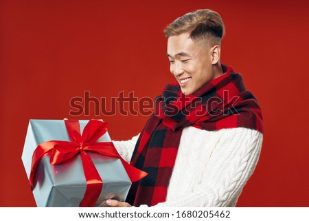 A man on a red background with a gift box in his hand is smiling at the camera