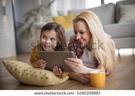 Time for favorite movies. Mother and daughter at home using digital tablet.