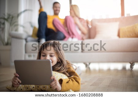  Time for cartoon. Family at home. Little girl lying on floor and using digital tablet. focus is on foreground.
