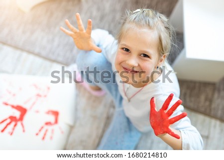 Adorable cute caucasian little blond girl enjoy having fun painting with brush, finger and palm paint at home indoors. Cheerful happy kids smiling drawing masterpiece art picture. Messy dirty room