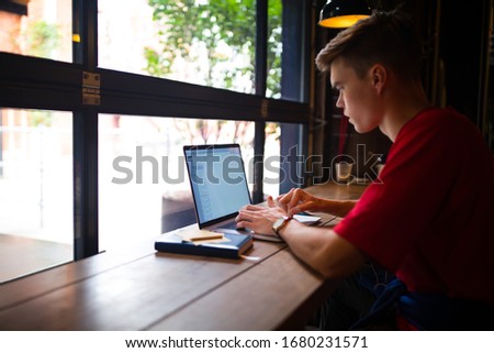 Stylish hipster guy skilled freelance social media content writer working on pc laptop computer while sitting in coffee shop near window with copy space. Man create account via notebook 