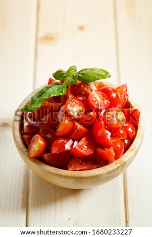 red cherry tomatoes and basil leaf in wooden bowl on wooden background