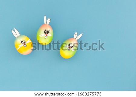 Colorful painted easter eggs with funny bunny ears and cartoon faces on light blue background