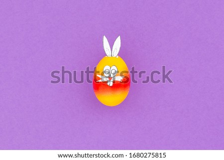Colorful painted easter egg with funny bunny ears and cartoon face on purple background