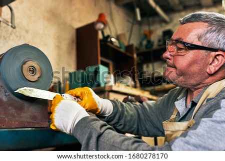 Closeup side view image of adult man manufacturing in his workshop. Worker man sharpens the knife in the repair shop.