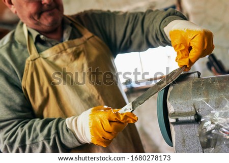 Closeup image of worker adult man manufacturing in his workshop. Confident man sharpens the knife in repair shop.