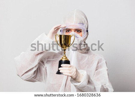 female doctor in protection suit and glasses with mask holds golden cup