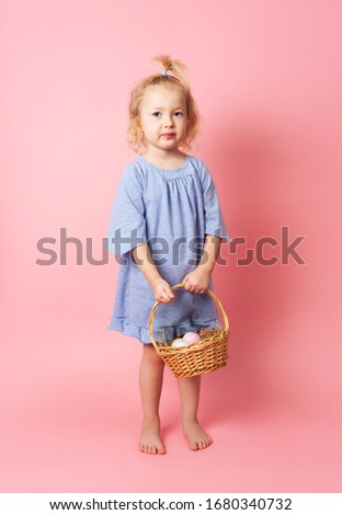 Happy Easter: a little girl in a blue dress holds a basket of eggs in her hands.