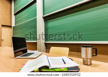 Photo of laptop on professor desk with tumbler and lesson plan 