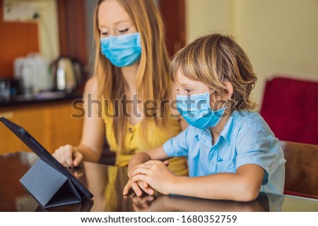 Boy studying online at home using a tablet. Mom helps him learn. Mom and son in medical masks to protect against coronovirus. Studying during quarantine. Global pandemic covid19 virus